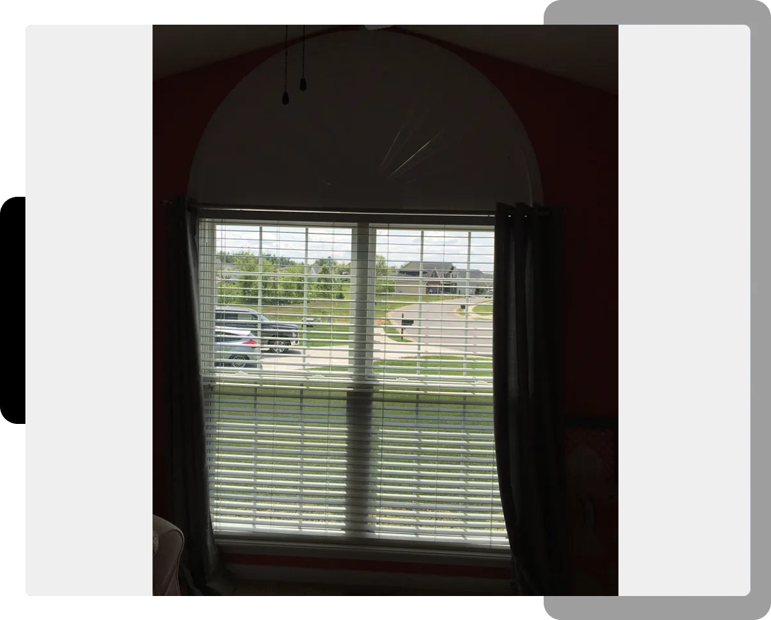 A window with blinds open and cars parked in the background.